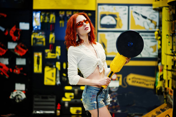 Red haired model posed with large angle grinder at store or hous - Zdjęcie, obraz
