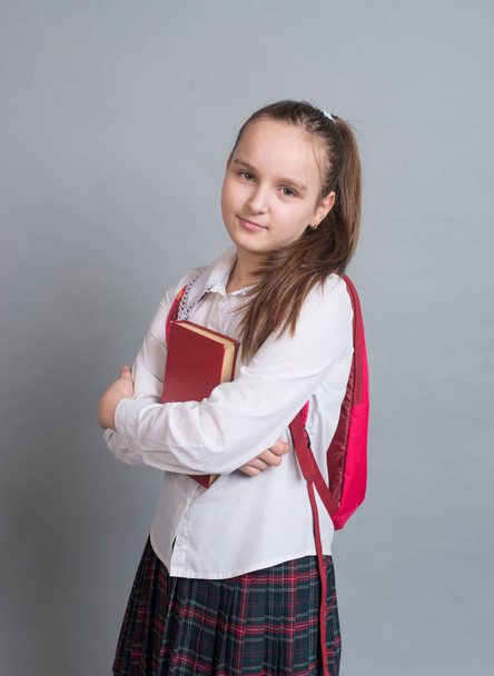 Schoolgirl in uniform stands with book and backpack  - Φωτογραφία, εικόνα