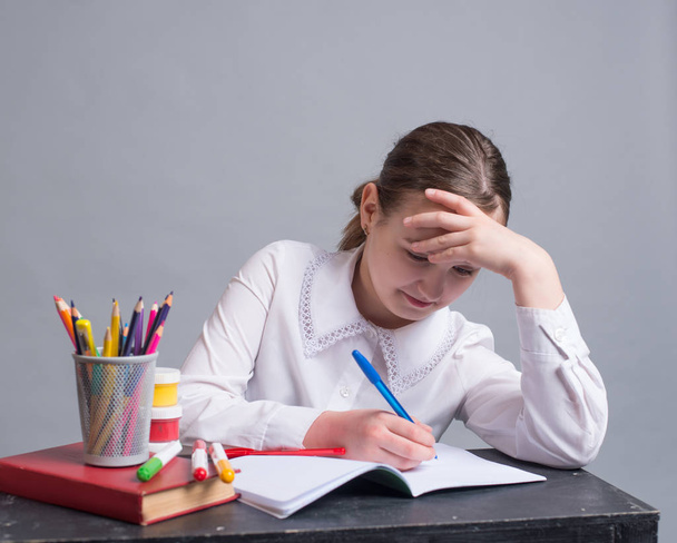 A schoolgirl sits at her desk and does homework - Foto, imagen