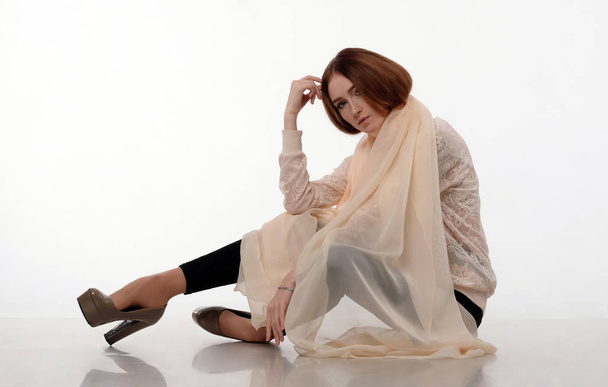 Young girl in beige shawl sits on the floor. - 写真・画像
