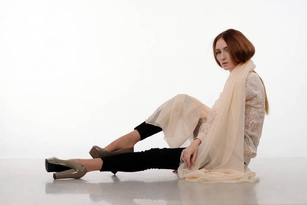 Beautiful woman in creme shawl sits on the floor. - Foto, Imagen