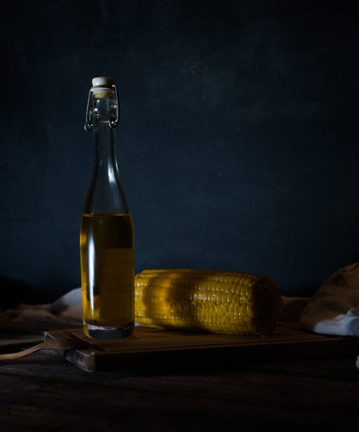 Bottles with oil, herbs and spices at wooden table on black background - 写真・画像