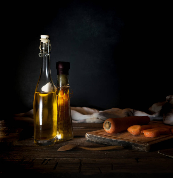 Bottles with oil, herbs and spices at wooden table on black background. - Фото, зображення