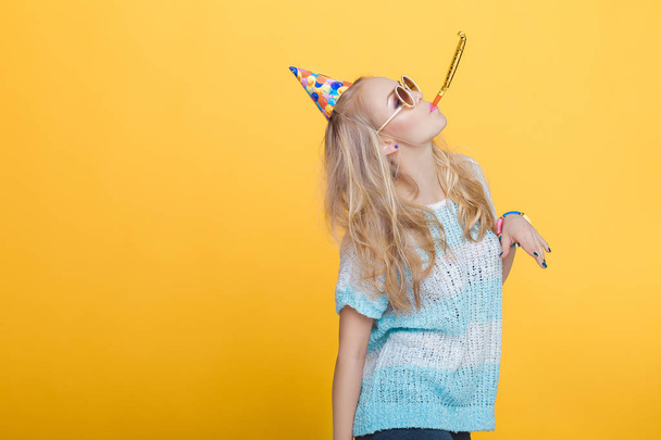 portrait of funny blond woman in birthday hat and blue shirt on yellow background. Celebration and party. - Valokuva, kuva