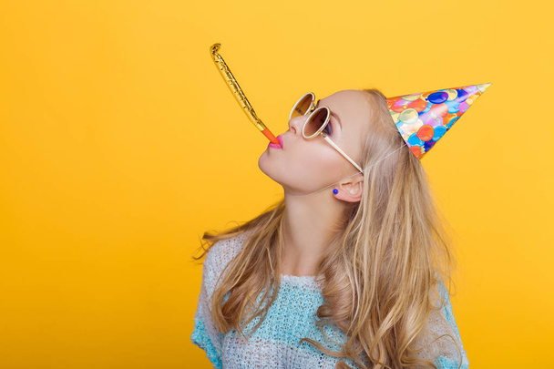 Portret van grappige Blonde vrouw in verjaardag hoed en blauw shirt op gele achtergrond. Feest en feest. - Foto, afbeelding
