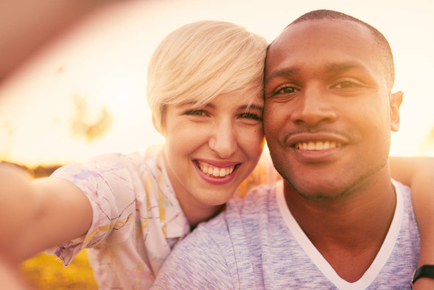 Mixed race couple of millennial in a grass field taking a selfie with a smartphone - Foto, Imagen