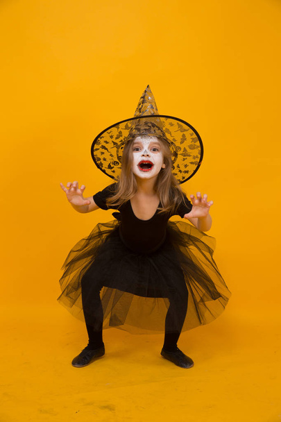 Small girl in Halloween witch costume, orange background. - Photo, image