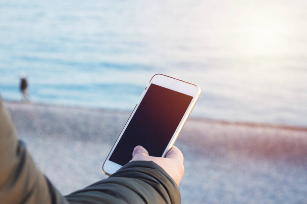 a male hand keeping a smart phone on the sea ocean background, p - Φωτογραφία, εικόνα