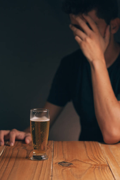 Concept of alcoholism. Sad man at the table with a glass of beer in a dark room. - Photo, image