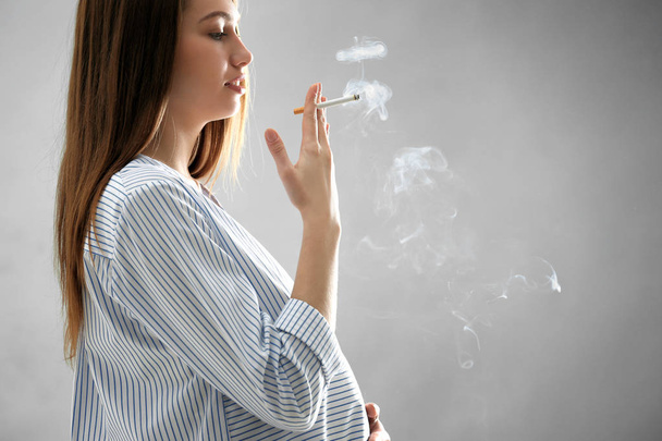 Pregnant woman smoking cigarette on grey background - Foto, immagini