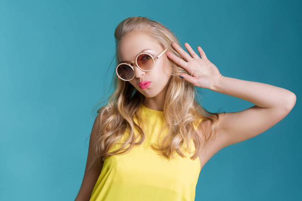 portrait of beautiful blond woman in sunglasses and yellow shirt on blue background. Carefree summer. - Φωτογραφία, εικόνα