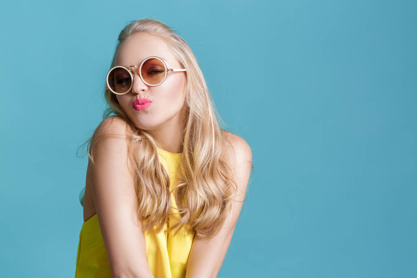 portrait of beautiful blond woman in sunglasses and yellow shirt on blue background. Carefree summer. - Photo, Image