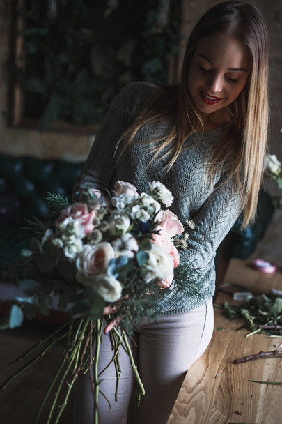Florist at work: pretty young blond woman holds fashion modern bouquet of different flowers - Fotó, kép