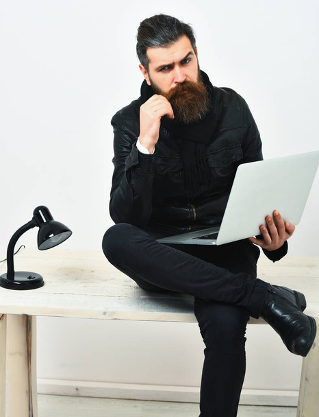 Bearded brutal caucasian hipster sitting on table with laptop - Photo, Image