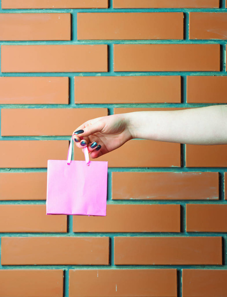 pink shopping bag in female hand on brick wall - 写真・画像