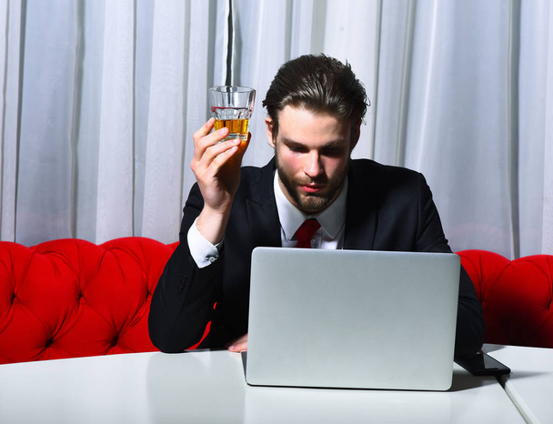 bearded man, businessman holding glass of whiskey works at laptop - Photo, image