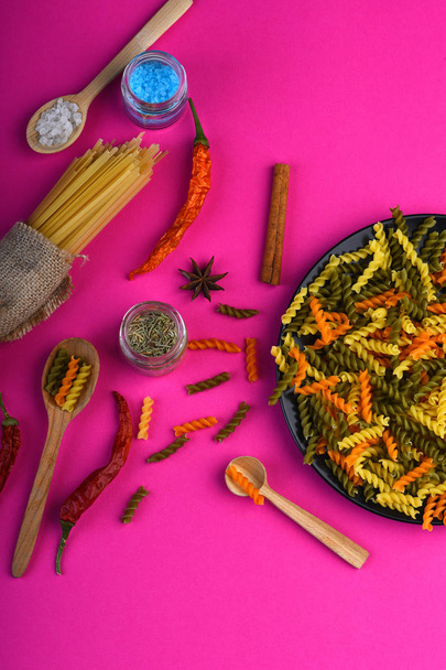 Colorful dried fusilli pasta on black plate and spaghetti bunch - Foto, Bild