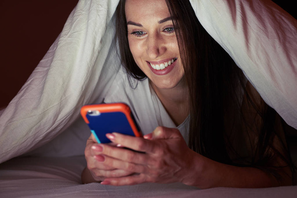 Girl under blanket at night with a smartphone - Zdjęcie, obraz