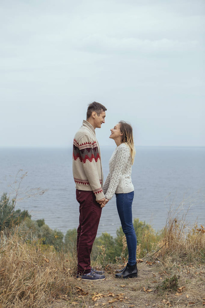 Feliz pareja pensativa de pie en un acantilado cerca del mar abrazando cada uno
 - Foto, Imagen