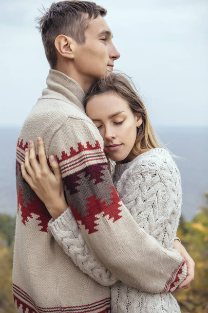 Feliz pareja pensativa de pie en un acantilado cerca del mar abrazando cada uno
 - Foto, Imagen