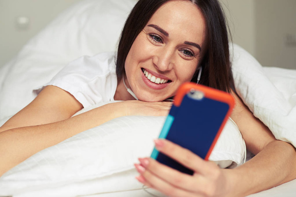 Brunette using telephone while lying on the pillow - Photo, Image