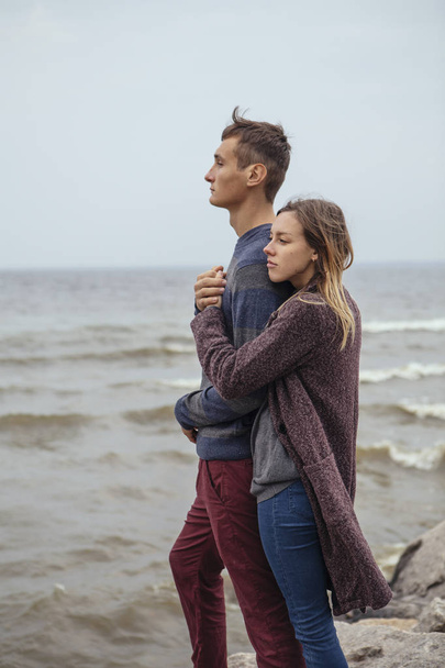 Feliz pareja pensativa de pie en una playa de roca cerca de abrazo al mar
 - Foto, imagen