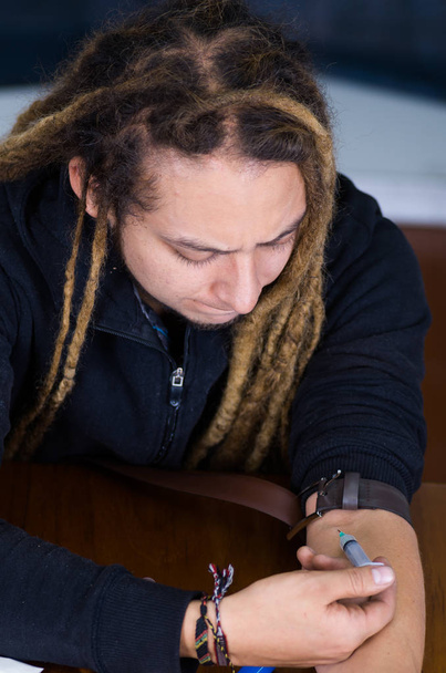 Man with drug addiction sitting down injecting narcotics into arm using syringe - Valokuva, kuva