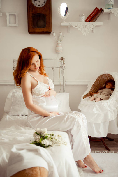 Femme enceinte aux cheveux roux en robe blanche dans la chambre des enfants
 - Photo, image