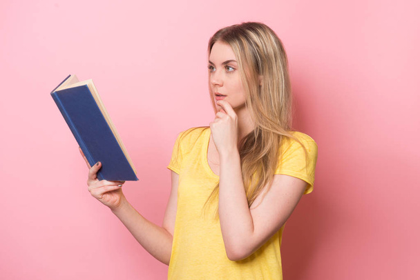 Girl reading a book and thinking near pink wall - Φωτογραφία, εικόνα