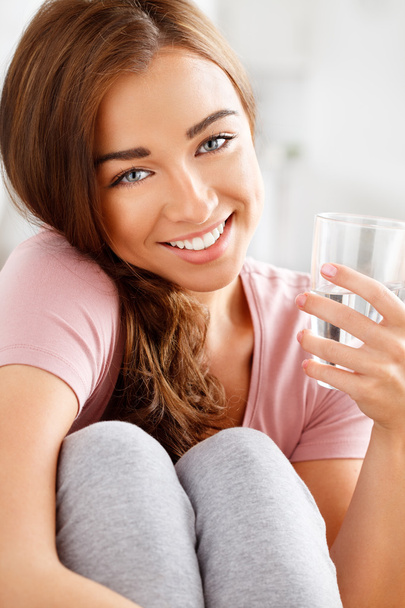 Close-up portrait of an attractive young woman smiling and holding a glass of water - Foto, immagini