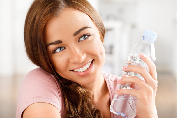 Healthy young woman holding a bottle of water and smiling - Fotoğraf, Görsel