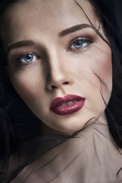 Widow in veils, portrait of young brunette woman against a dark background. Mysterious bright image of a woman with professional makeup. Veil on the woman's face. - Foto, Imagem
