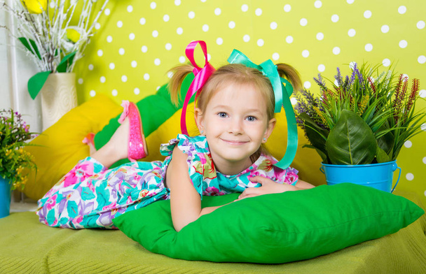 Porträt eines aufgeweckten Mädchens in einem farbenfrohen BaumwollOverall und mit Schleifen auf dem Kopf - Foto, Bild