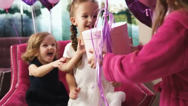 Little girl giving present box with baloons to pretty girls. back view - Footage, Video
