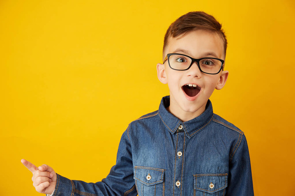 A little boy shows his finger to the side against the yellow background - Foto, afbeelding