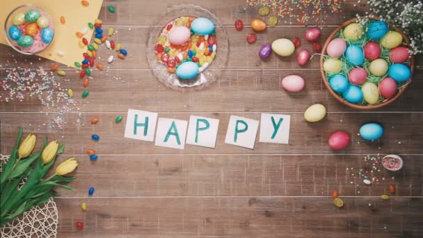 Man put words Happy Easter on table decorated with easter eggs. Top view - Video