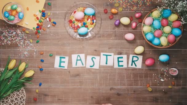 Man puts word Easter on table decorated with easter eggs. Top view - Video
