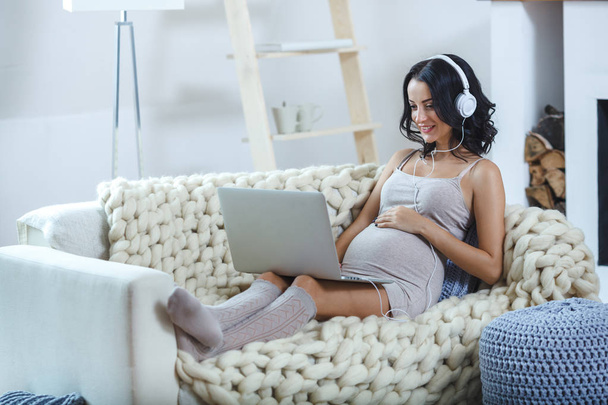 Beautiful young pregnant woman with laptop sitting on sofa at home - Foto, immagini