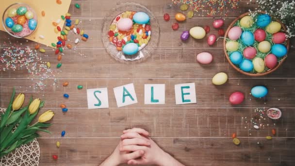 Man puts word Sale on table decorated with easter eggs. Top view - Video