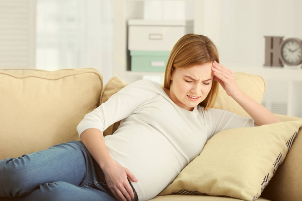 Pregnant woman suffering from headaches while lying on sofa at home - Fotoğraf, Görsel