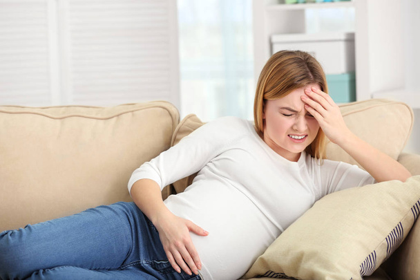 Pregnant woman suffering from headaches while lying on sofa at home - Foto, Bild