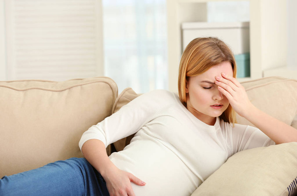 Pregnant woman suffering from headaches while lying on sofa at home - Foto, immagini