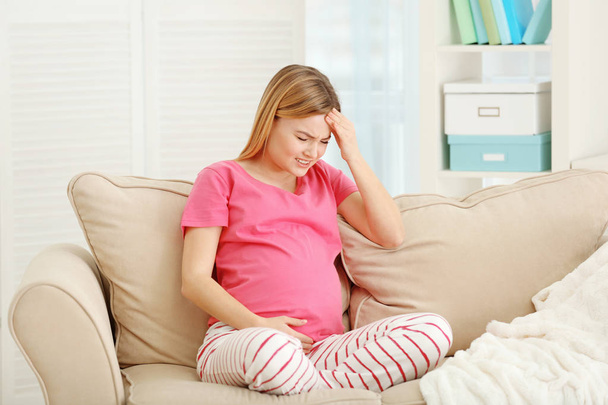 自宅のソファーに座りながら頭痛に苦しんで妊娠中の女性 - 写真・画像