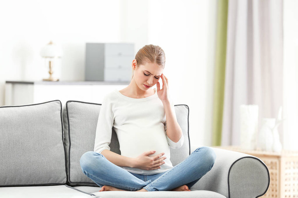 Pregnant woman suffering from headaches while sitting on sofa at home - Fotoğraf, Görsel