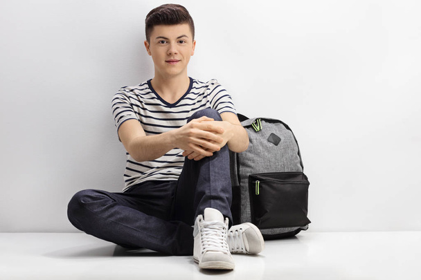 Teenager sitting on the floor next to a backpack - Foto, imagen