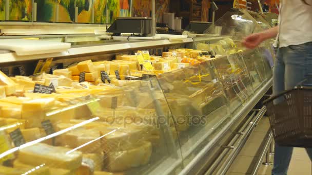 junge Frau mit Einkaufswagen kommt zum Kühlschrank im Geschäft und nimmt Ware aus diesem. Mädchen wählen Käse im Kühlregal im Laden aus und legen ihn in den Korb - Filmmaterial, Video