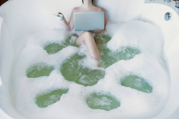 A girl in a jacuzzi in foam works at the computer and rests.  - Fotoğraf, Görsel