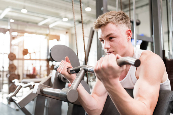 Young man in gym working out, using weights machine for arms. - Photo, image