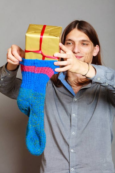 Guy putting wrapped gift in knitted christmas sock - Фото, зображення