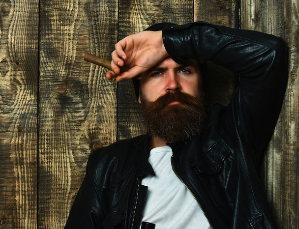 Bearded brutal caucasian hipster holding bottle and smoking cigar - Фото, изображение